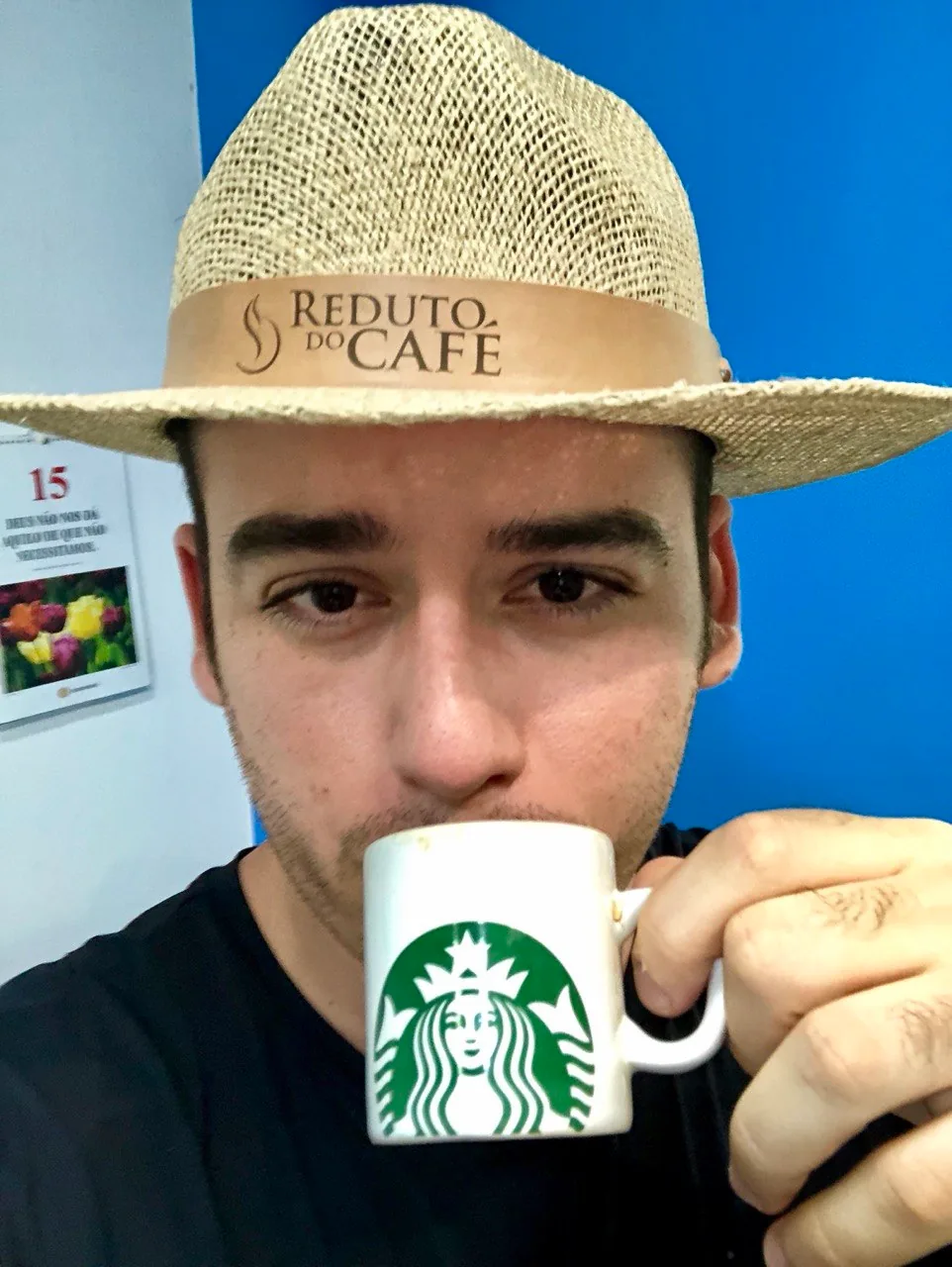 Pessoa usando chapéu de palha com a inscrição Reduto do Café e segurando uma xícara branca.