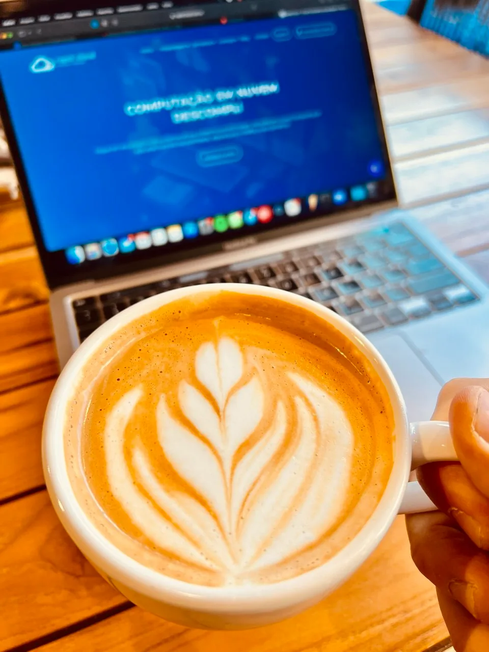 Xícara com latte art em primeiro plano e notebook aberto no site da Rapid Cloud ao fundo.