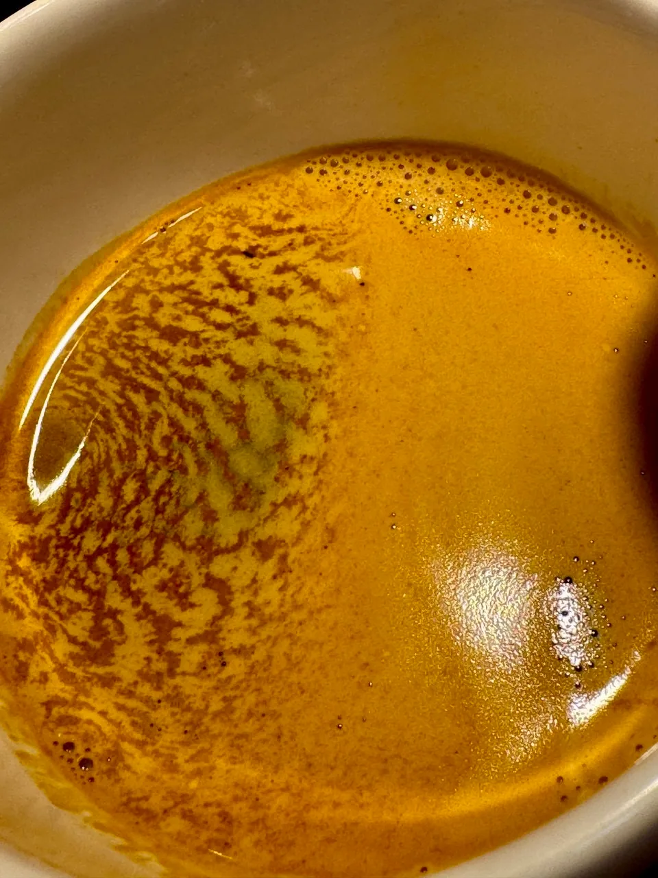Close da crema dourada de um espresso em uma xícara branca.