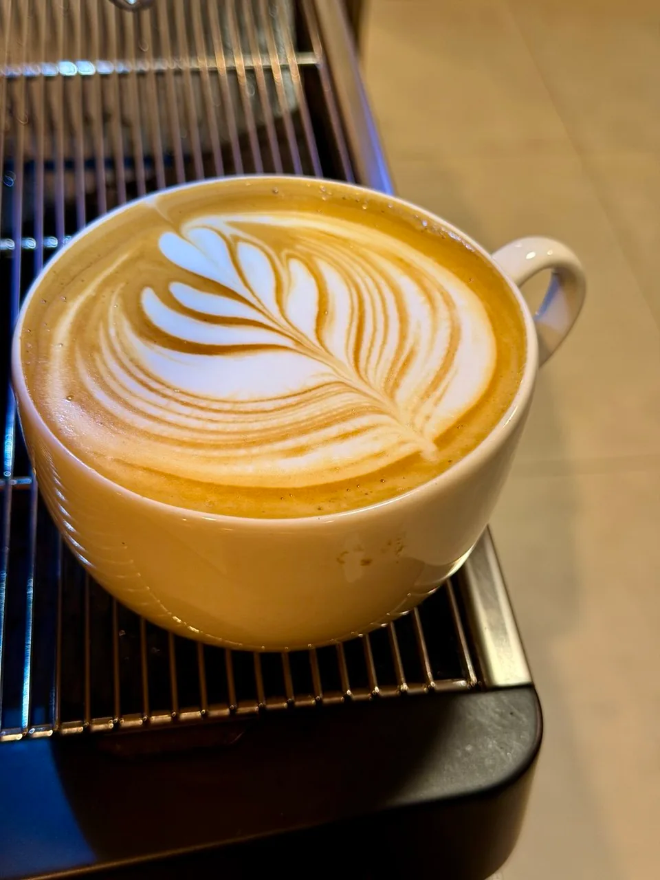 Xícara de café com latte art de folhas e corações apoiada na bandeja da máquina de espresso.