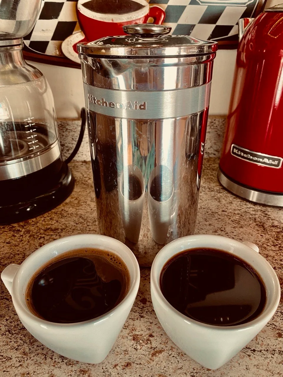 Prensa francesa de inox KitchenAid com duas xícaras brancas de café à frente.