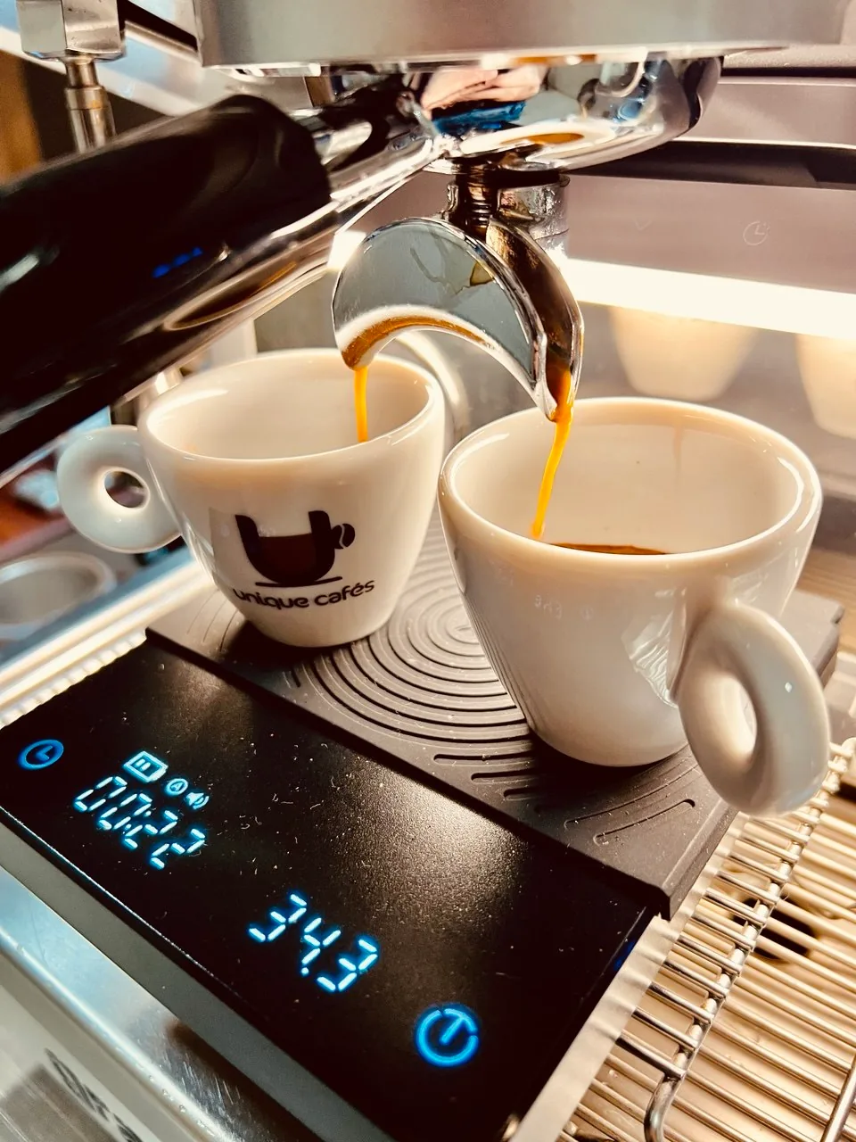 Dois espressos sendo extraídos em xícaras brancas sobre uma balança digital.