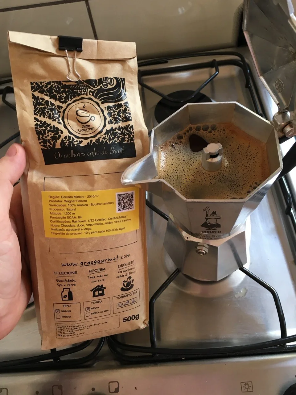 Cafeteira italiana Bialetti aberta no fogão, ao lado de um pacote da Grão Gourmet.