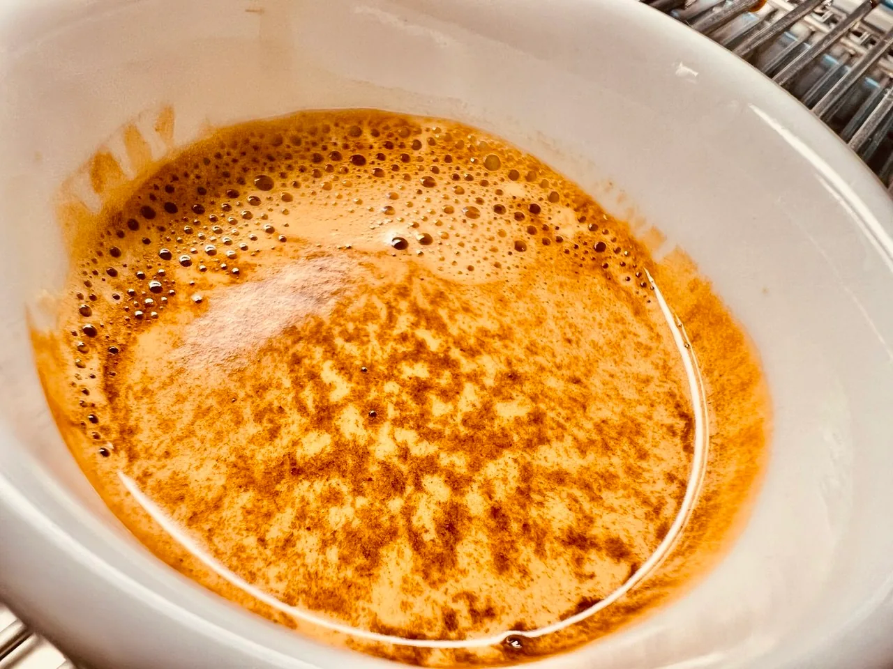 Vista de perto da crema de um espresso, com pequenas bolhas e marcas mais escuras.