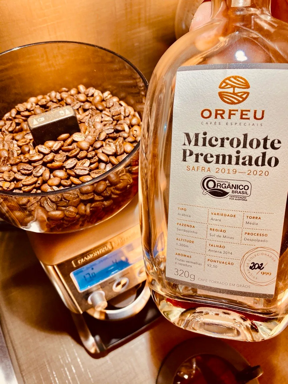 Garrafa de café Orfeu Microlote Premiado ao lado de um moinho com grãos no reservatório.