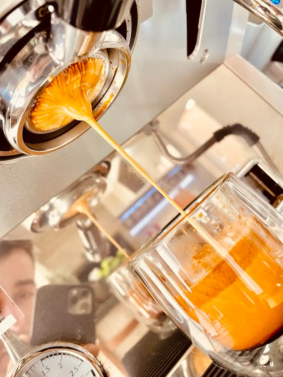 Espresso escorrendo de um porta-filtro sem fundo para um copo de vidro.