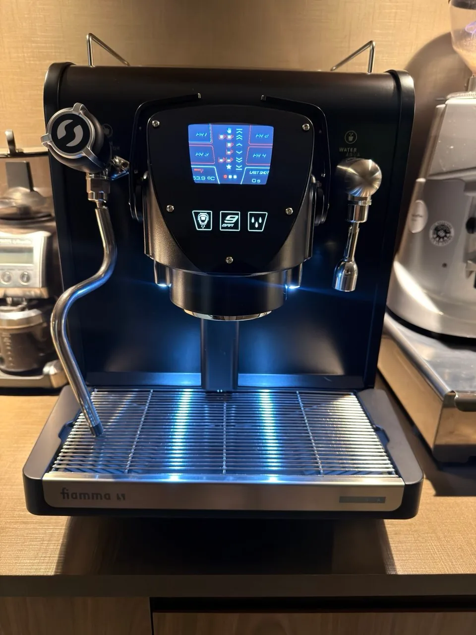 Vista frontal da máquina de espresso Fiamma, com painel digital e iluminação azul na bandeja.